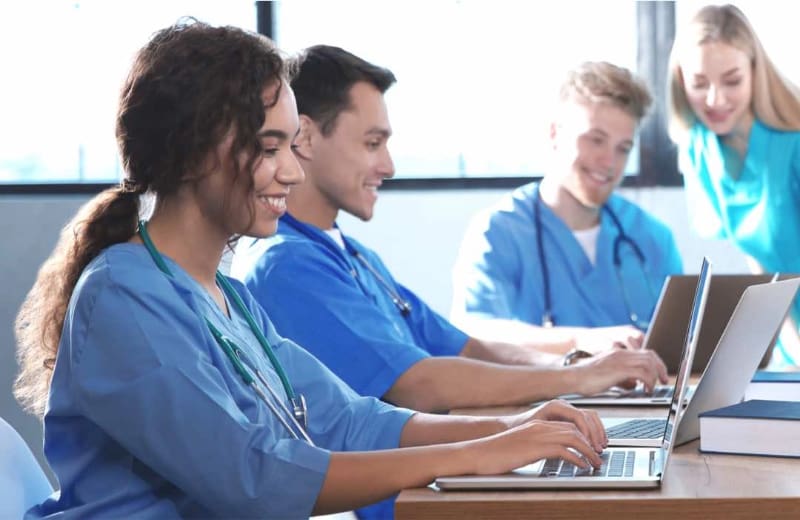 Students of healthcare wearing scrubs working at laptops together