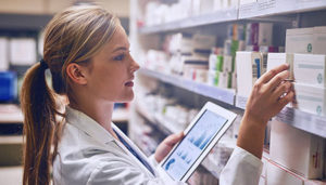 young pharmacy technician lab coat holding an iPad while looking at a small box