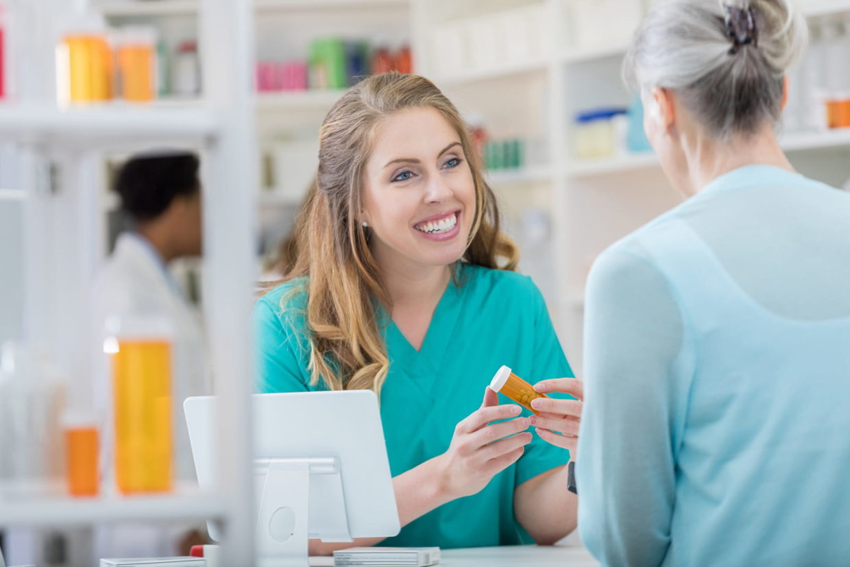 Smiling young Caucasian female pharmacist talks with senior Caucasian female patient. The patient is asking the pharmacist questions about her medication.